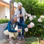 Two women admire pink flowers in a garden.